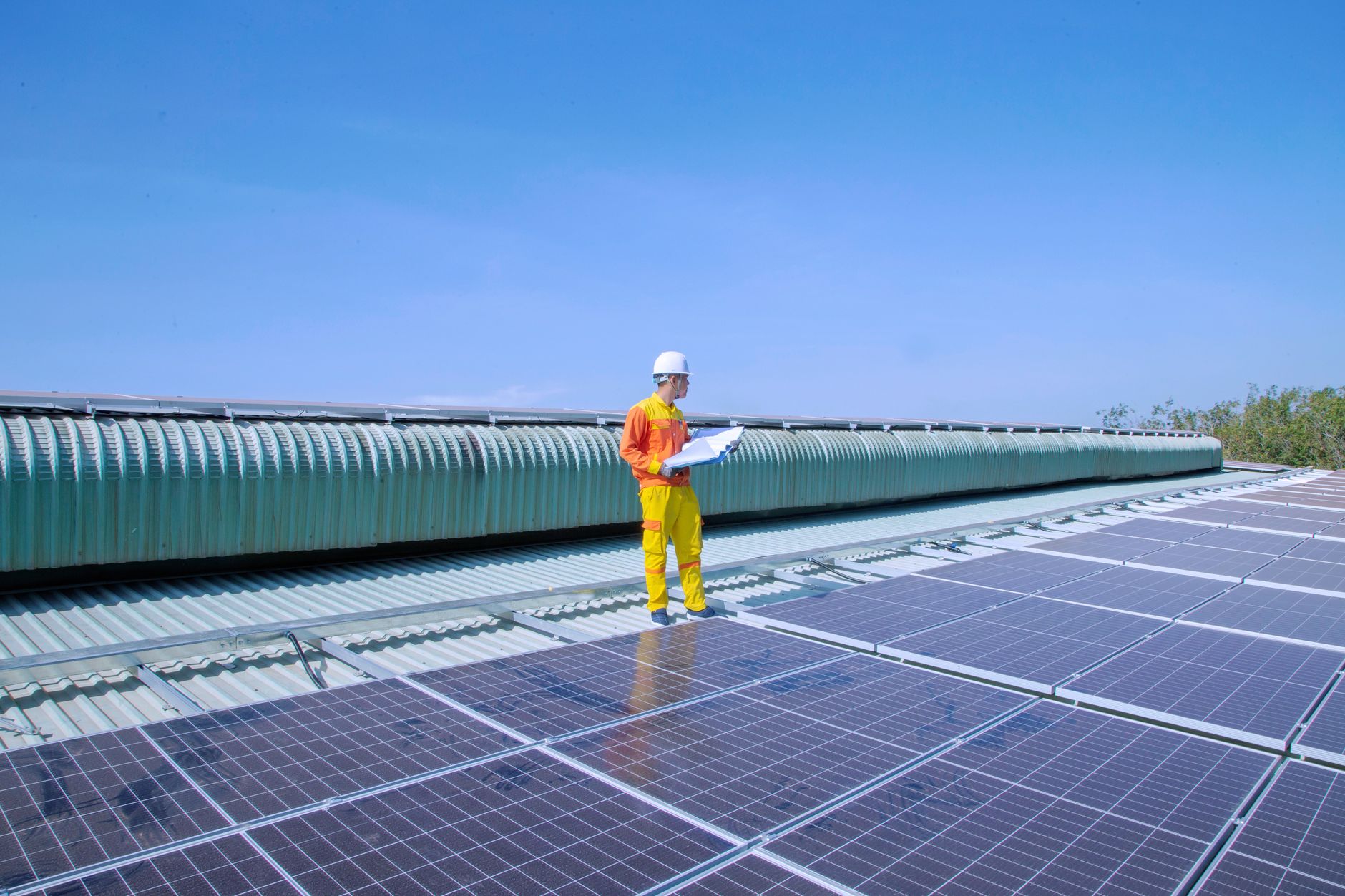 Radnik u zaštitnoj opremi sa planom rada na krovu pokrivenom solarnim panelima