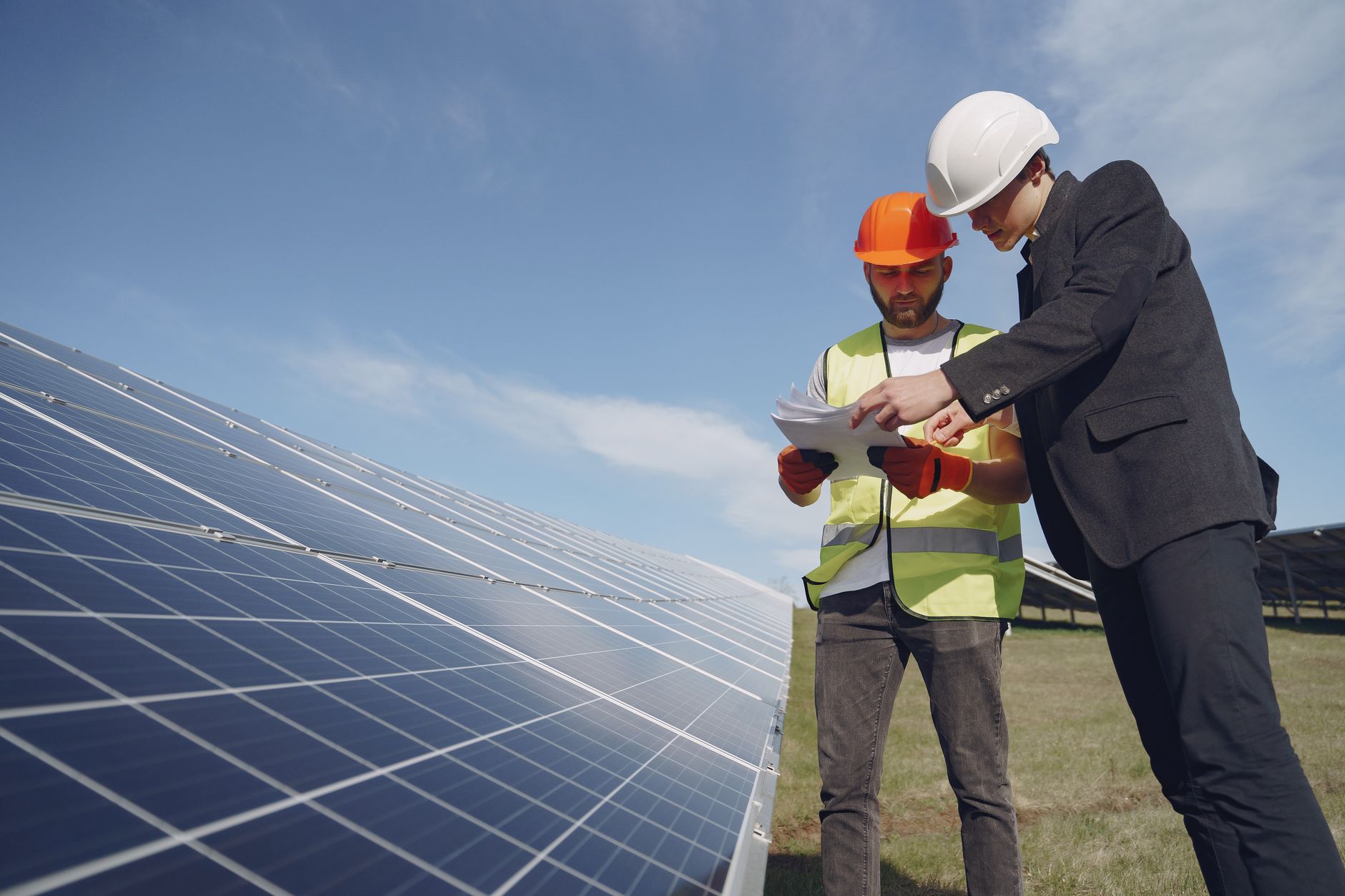 Dva stručnjaka u kacigama pregledaju plan rada pored redova solarnih panela na polju